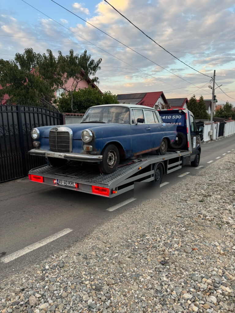 Mașină clasică albastră încărcată pe o platformă auto pe o stradă.