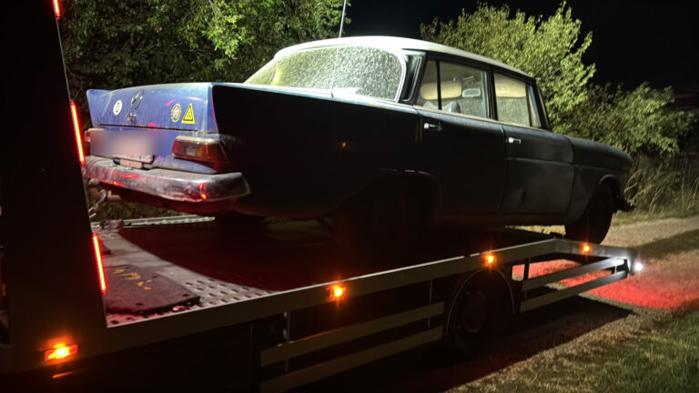 Mașină clasică încărcată pe o platformă auto, fotografiată noaptea.